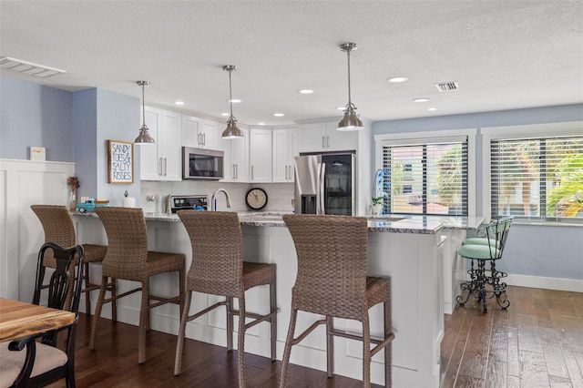 kitchen featuring pendant lighting, white cabinetry, a kitchen breakfast bar, light stone counters, and stainless steel appliances