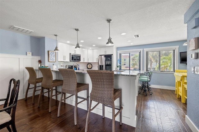 kitchen with a breakfast bar, white cabinetry, stainless steel appliances, light stone counters, and kitchen peninsula