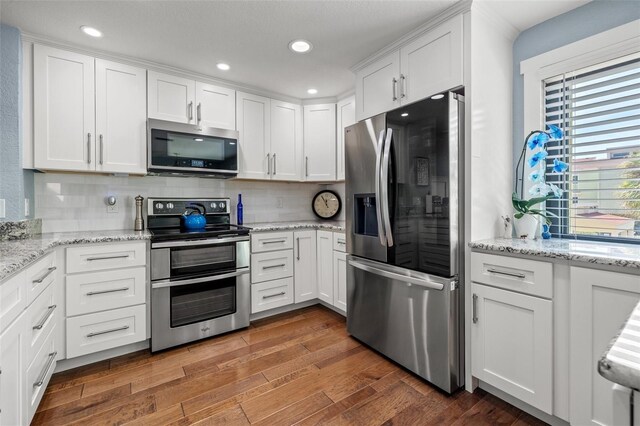 kitchen featuring appliances with stainless steel finishes, dark hardwood / wood-style flooring, white cabinets, light stone countertops, and backsplash