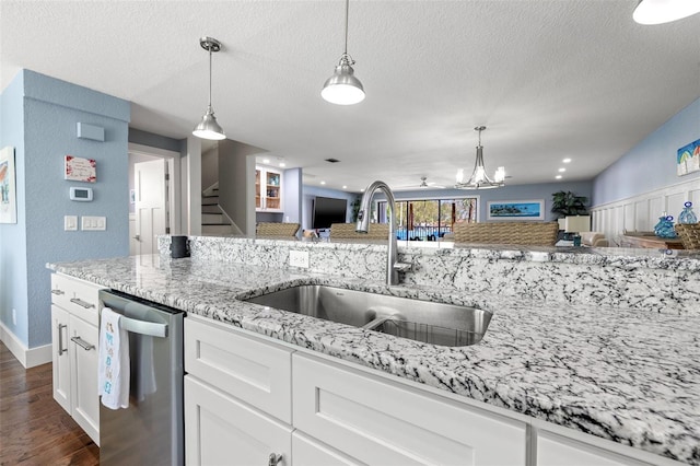 kitchen with decorative light fixtures, white cabinetry, sink, stainless steel dishwasher, and light stone counters