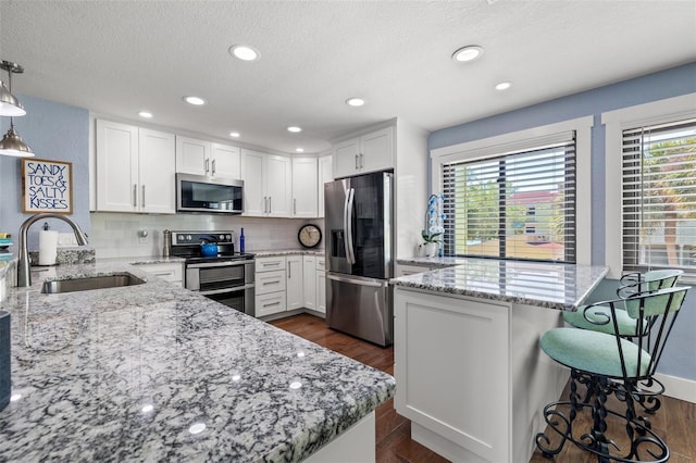 kitchen with sink, white cabinetry, light stone counters, pendant lighting, and stainless steel appliances