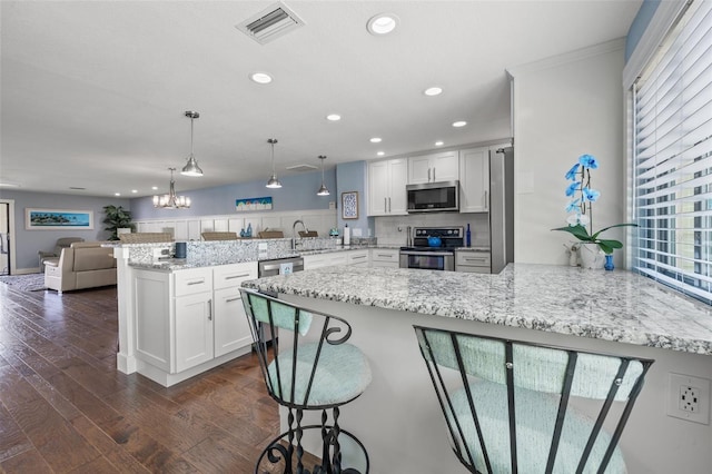 kitchen with white cabinetry, stainless steel appliances, kitchen peninsula, and hanging light fixtures