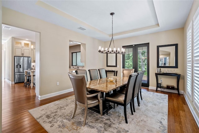 dining area featuring a raised ceiling, dark hardwood / wood-style floors, and a chandelier