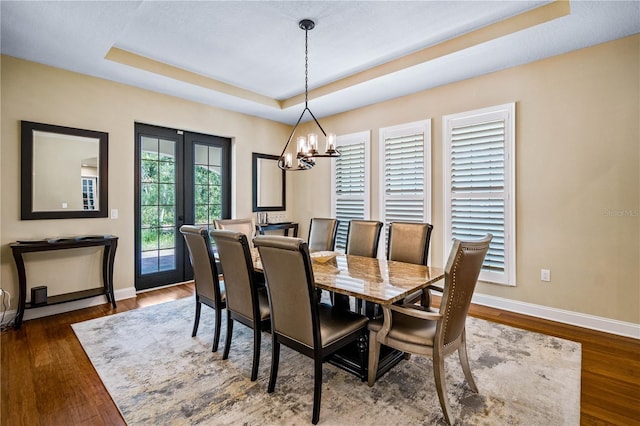 dining area featuring french doors, a tray ceiling, dark hardwood / wood-style flooring, and a notable chandelier