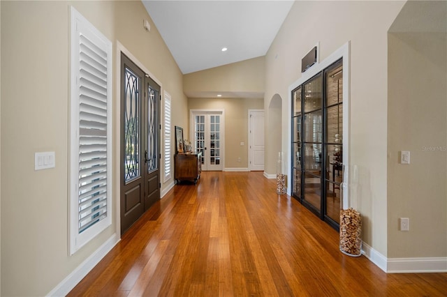 corridor with wood-type flooring, high vaulted ceiling, and french doors