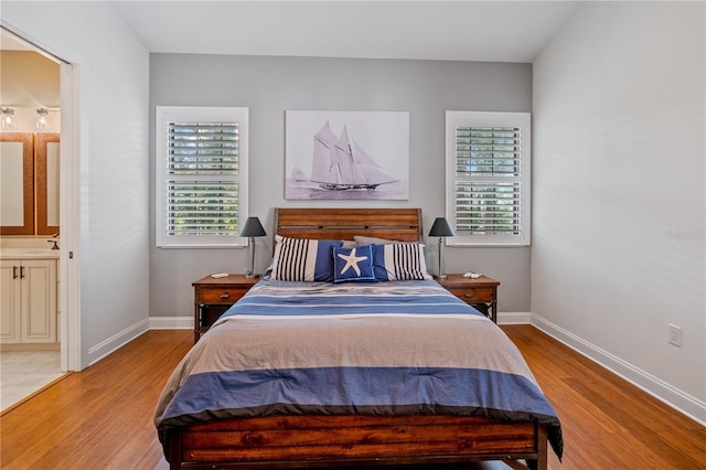 bedroom with ensuite bathroom, multiple windows, and light hardwood / wood-style flooring