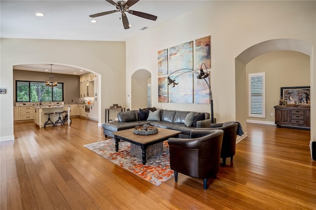 living room with high vaulted ceiling, ceiling fan, and light hardwood / wood-style flooring