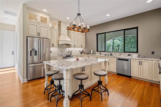 kitchen with light stone counters, appliances with stainless steel finishes, a kitchen island, custom range hood, and pendant lighting