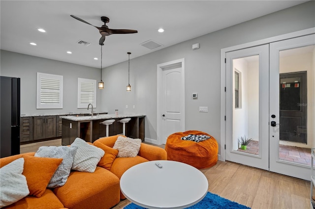 interior space featuring light hardwood / wood-style flooring, dark brown cabinetry, a center island with sink, decorative light fixtures, and french doors