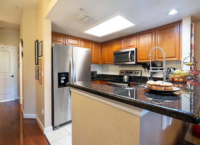 102 Brent Cir, Oldsmar, FL 34677 - kitchen featuring stainless steel appliances, a peninsula, brown cabinets, tasteful backsplash, and baseboards