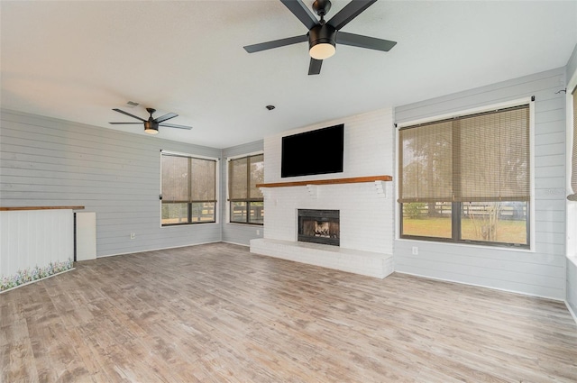 unfurnished living room with a fireplace, ceiling fan, and light wood-type flooring