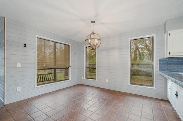 unfurnished dining area with wooden walls, a textured ceiling, and a chandelier