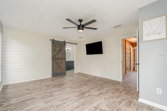 unfurnished living room featuring ceiling fan, a barn door, light hardwood / wood-style floors, and a textured ceiling