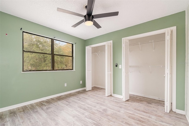 unfurnished bedroom featuring ceiling fan, two closets, light hardwood / wood-style floors, and a textured ceiling