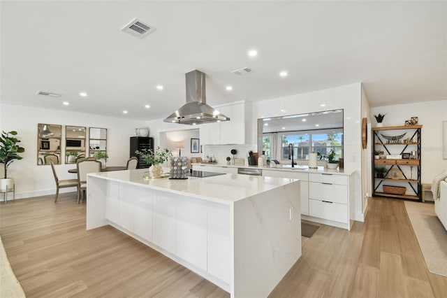 kitchen with white cabinetry, island exhaust hood, light hardwood / wood-style floors, and a spacious island