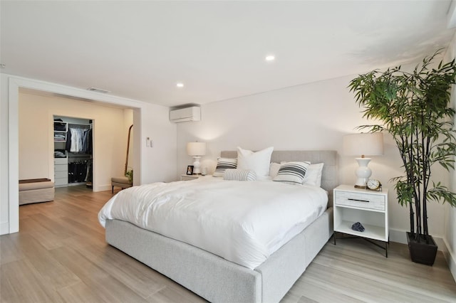 bedroom featuring a spacious closet, a wall unit AC, and light wood-type flooring