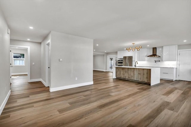 kitchen featuring pendant lighting, wall chimney range hood, a large island, white cabinetry, and light wood-type flooring