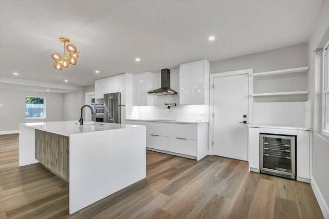 kitchen featuring white cabinetry, hanging light fixtures, heating unit, a center island with sink, and wall chimney exhaust hood