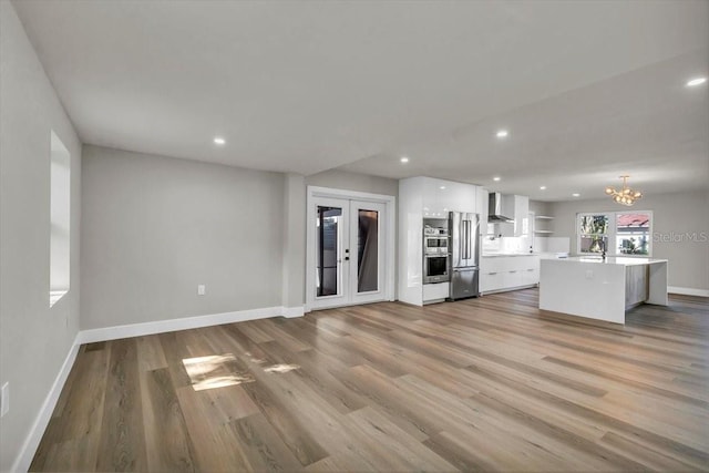 kitchen featuring wall chimney exhaust hood, white cabinetry, light wood-type flooring, a kitchen island, and stainless steel appliances