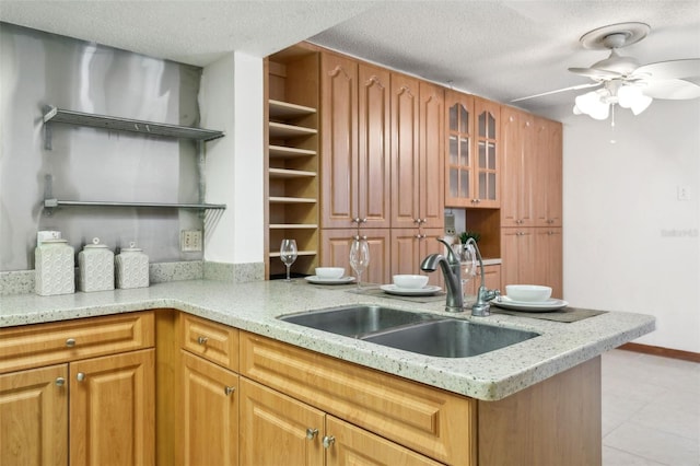 kitchen with ceiling fan, light stone countertops, sink, and a textured ceiling