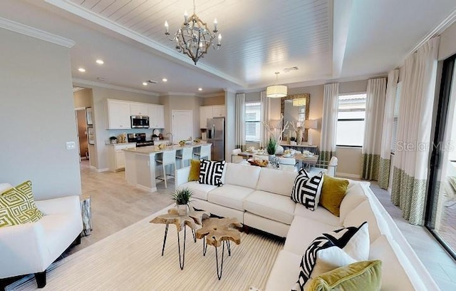 living room with ornamental molding, a chandelier, sink, and a raised ceiling