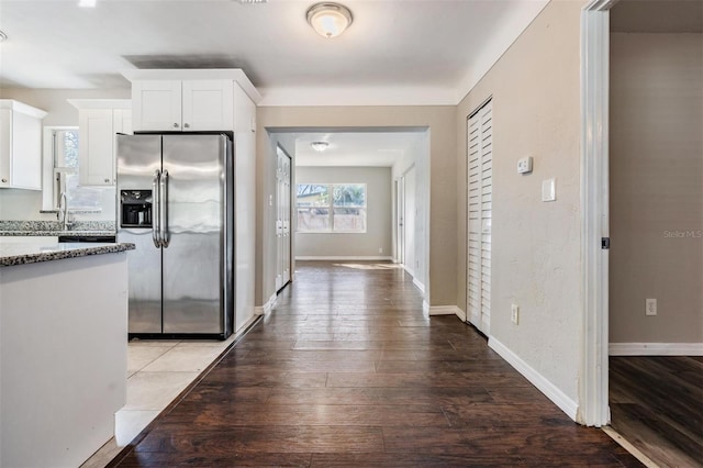 kitchen featuring stainless steel refrigerator with ice dispenser, sink, white cabinetry, light stone counters, and wood-type flooring