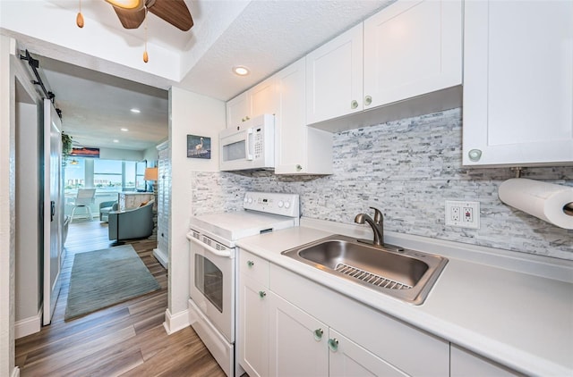 kitchen featuring tasteful backsplash, white cabinetry, wood-type flooring, sink, and white appliances