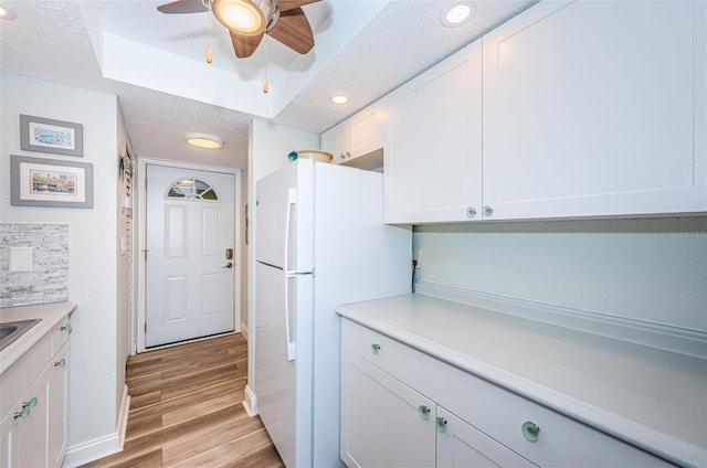 kitchen with a textured ceiling, light wood-type flooring, white cabinets, and white fridge