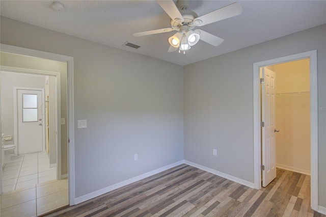 unfurnished bedroom featuring a walk in closet, ceiling fan, a textured ceiling, light wood-type flooring, and a closet