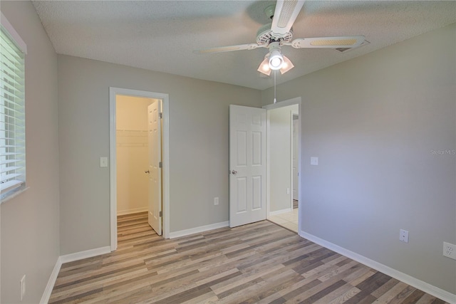 unfurnished bedroom with light hardwood / wood-style flooring, a walk in closet, ceiling fan, a textured ceiling, and a closet