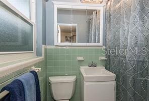 bathroom featuring vanity, toilet, and tile walls