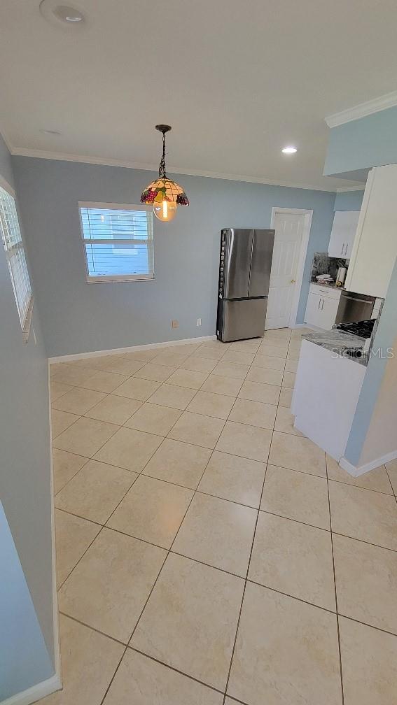 kitchen with decorative light fixtures, light tile patterned floors, ornamental molding, stainless steel fridge, and white cabinets