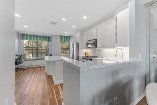 kitchen with stainless steel appliances, kitchen peninsula, light hardwood / wood-style flooring, and white cabinets