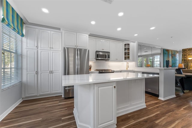 kitchen with appliances with stainless steel finishes, white cabinetry, sink, kitchen peninsula, and dark wood-type flooring