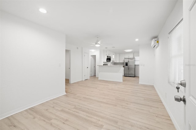 unfurnished living room featuring ceiling fan, a wall mounted air conditioner, and light wood-type flooring