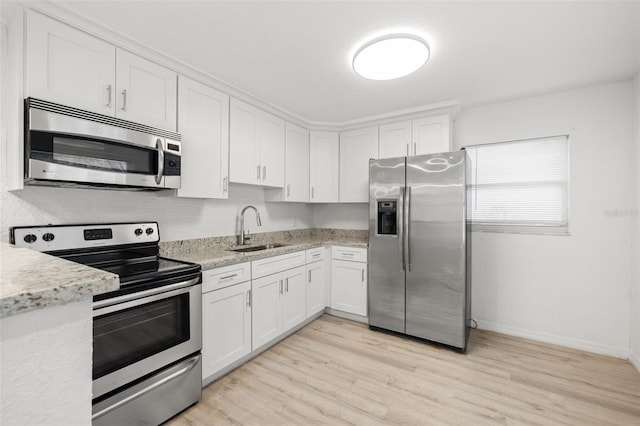 kitchen featuring sink, white cabinetry, light wood-type flooring, appliances with stainless steel finishes, and light stone countertops