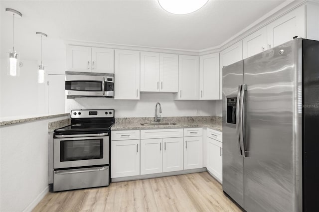 kitchen featuring appliances with stainless steel finishes, decorative light fixtures, sink, white cabinets, and light hardwood / wood-style floors