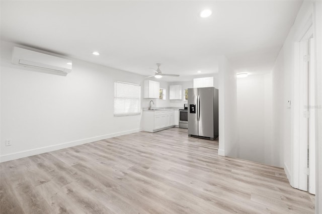 unfurnished living room featuring light wood-type flooring, ceiling fan, sink, and an AC wall unit