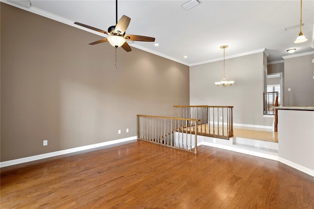 empty room featuring wood-type flooring, ornamental molding, and ceiling fan with notable chandelier