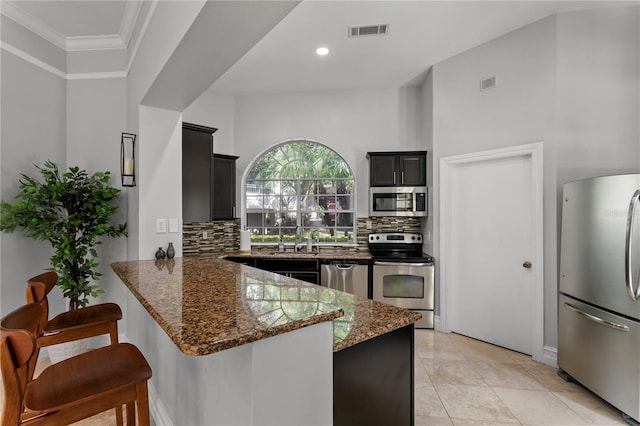 kitchen with appliances with stainless steel finishes, sink, dark stone countertops, decorative backsplash, and kitchen peninsula