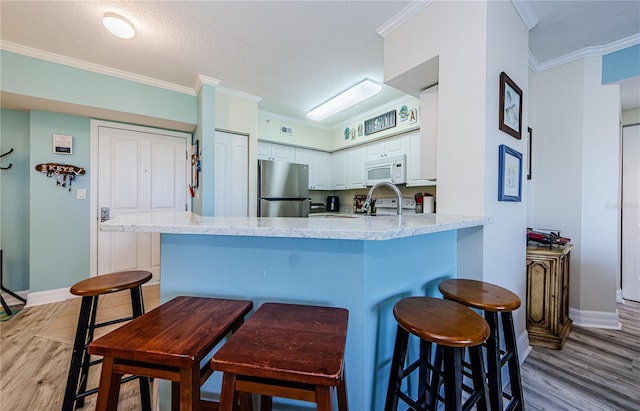 kitchen with crown molding, a kitchen breakfast bar, kitchen peninsula, white appliances, and white cabinets