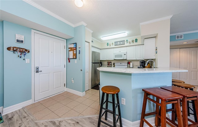 kitchen with white cabinetry, ornamental molding, a kitchen breakfast bar, kitchen peninsula, and white appliances