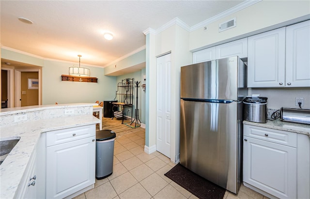 kitchen with light tile patterned floors, crown molding, stainless steel refrigerator, hanging light fixtures, and white cabinets