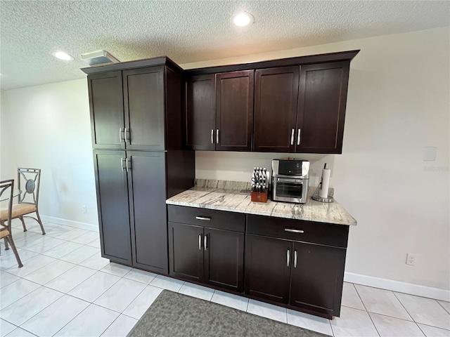 kitchen featuring light tile patterned flooring, light stone countertops, dark brown cabinets, and a textured ceiling