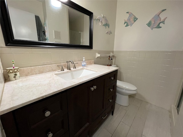 bathroom featuring vanity, tile walls, and toilet