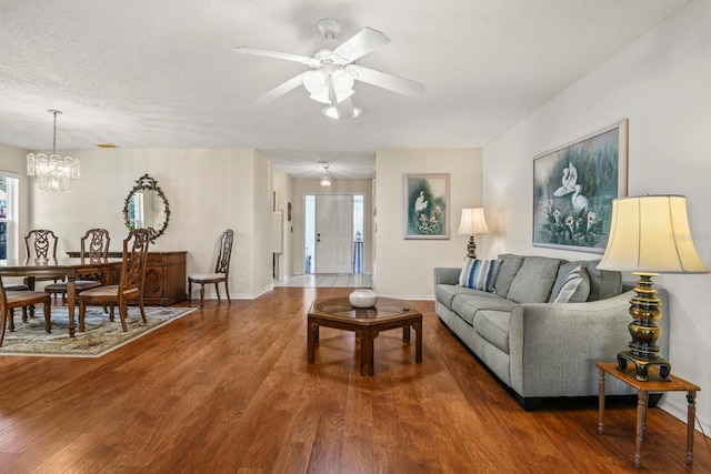 living room with ceiling fan with notable chandelier, dark hardwood / wood-style floors, and a textured ceiling