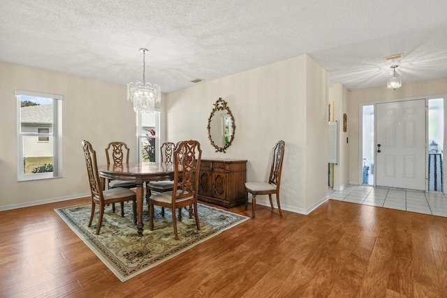 dining room with light wood-type flooring, a textured ceiling, and a notable chandelier