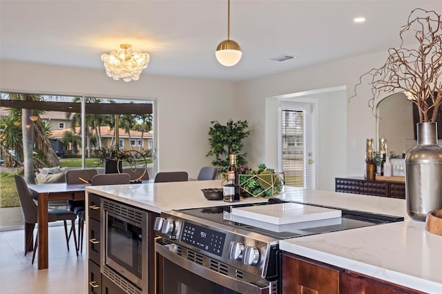 kitchen featuring appliances with stainless steel finishes, a healthy amount of sunlight, an inviting chandelier, and light stone counters