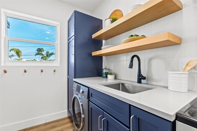 kitchen featuring blue cabinetry, washer / dryer, sink, light hardwood / wood-style flooring, and backsplash