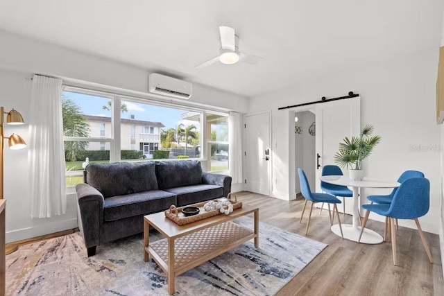 living room featuring ceiling fan, a barn door, a wall mounted air conditioner, and light wood-type flooring